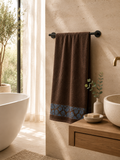 Absorbent brown cotton bath towel with floral border displayed on a modern towel stand