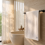 White cotton bath towel with an all-over floral damask pattern folded on a wooden bathroom shelf.