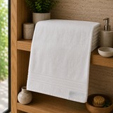 White cotton bath towel with woven border folded on a wooden bathroom shelf
