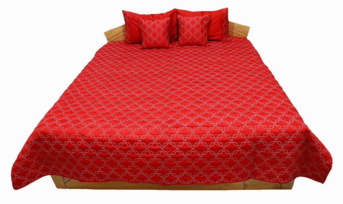 Red quilted double bedcover with a white diamond-lattice embroidery, angled view showing the matching pillow and cushion covers