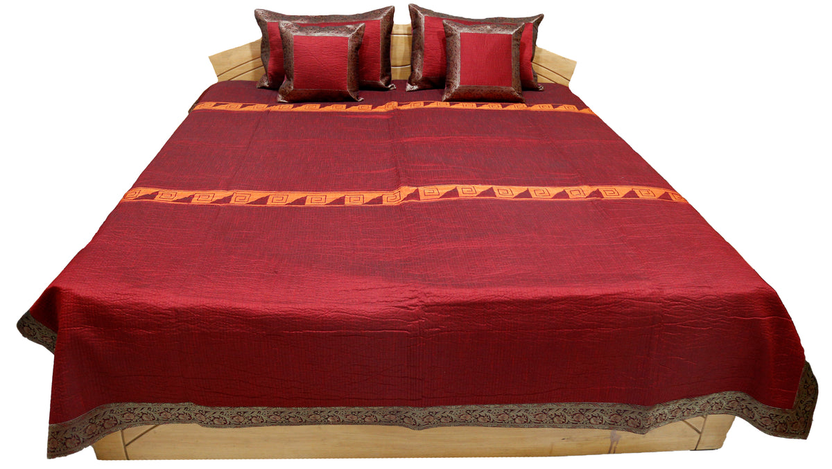 Maroon-red satin double bedcover with a grey-brown zari-brocade border, angled view on the bed