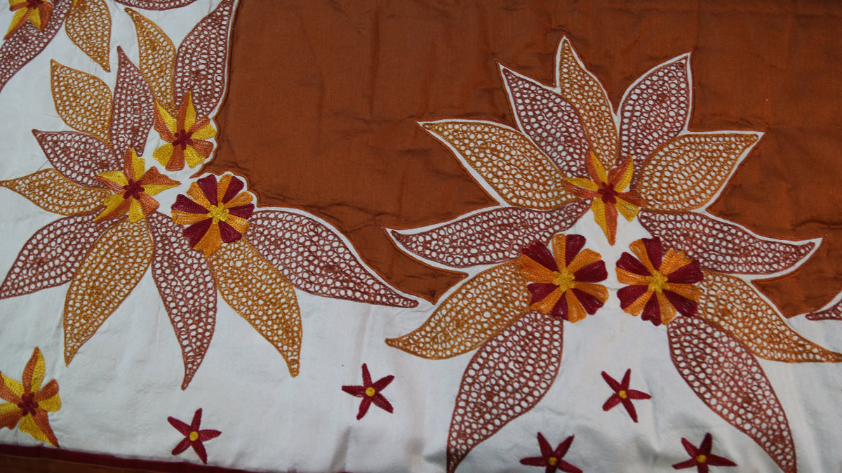 Close up of the rust brown fabric with large cream embroidered lily flowers
