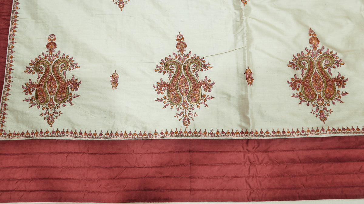 Close-up of the cream silk fabric with a maroon-gold paisley medallion embroidery and rust pleated border