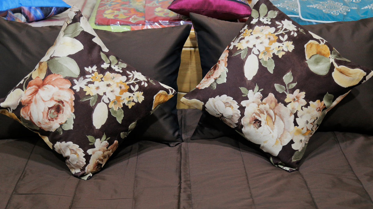 Close-up of two cream and peach rose print cushion covers on brown silk