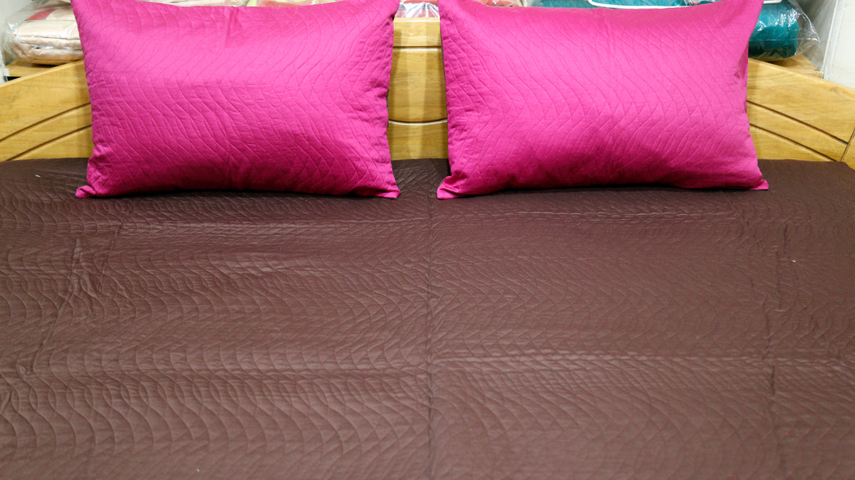 Close-up of magenta pillow covers on the aubergine quilted bedcover