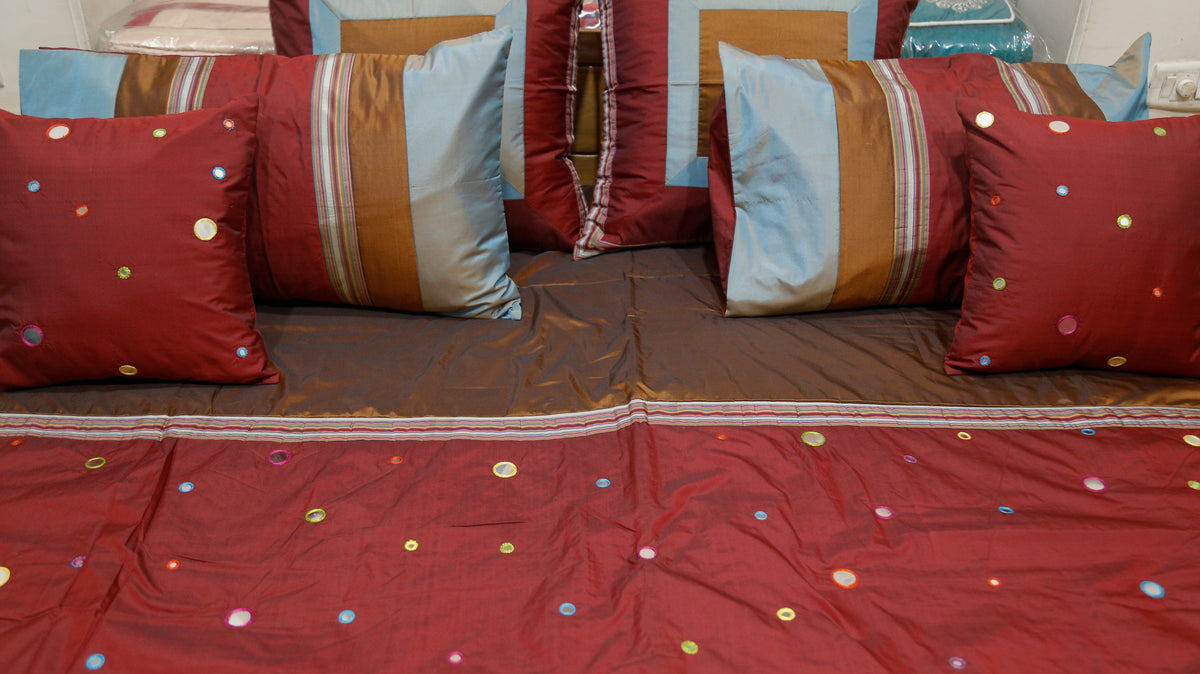 Close-up of coloured mirror work dots on maroon silk with striped cushion covers
