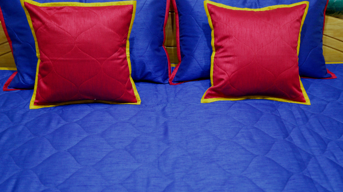 Close-up of crimson gold edged cushion covers on the royal blue quilted bedcover