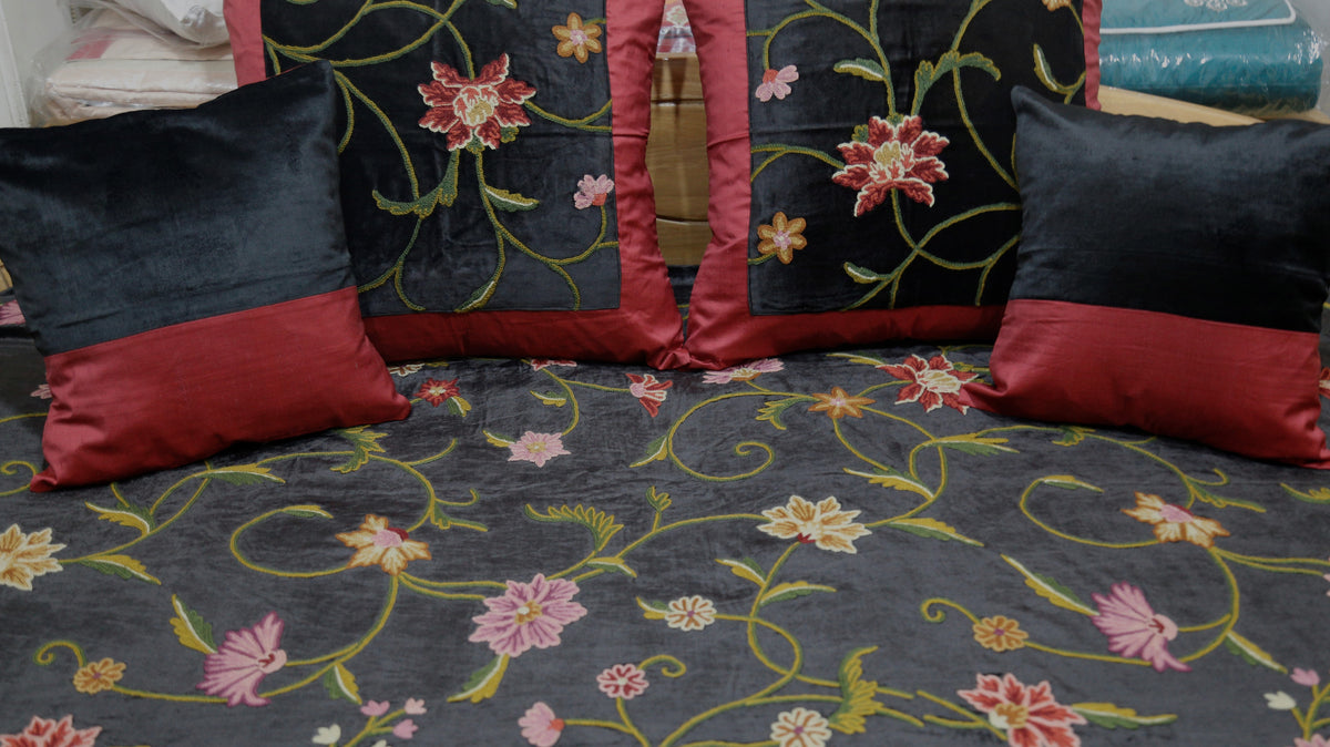 Close-up of the maroon and black velvet cushion covers against the floral-embroidered black bedcover