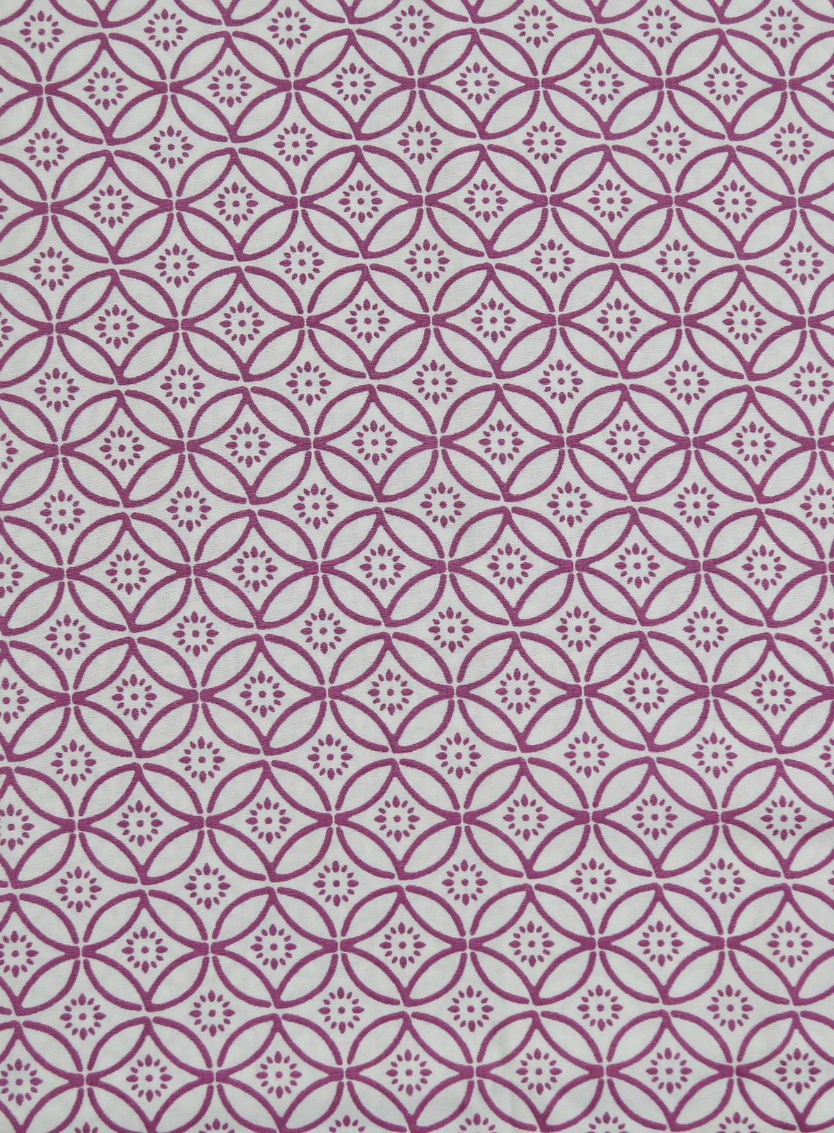 Close-up of magenta quatrefoil-circle geometric print fabric on a white cotton bedsheet