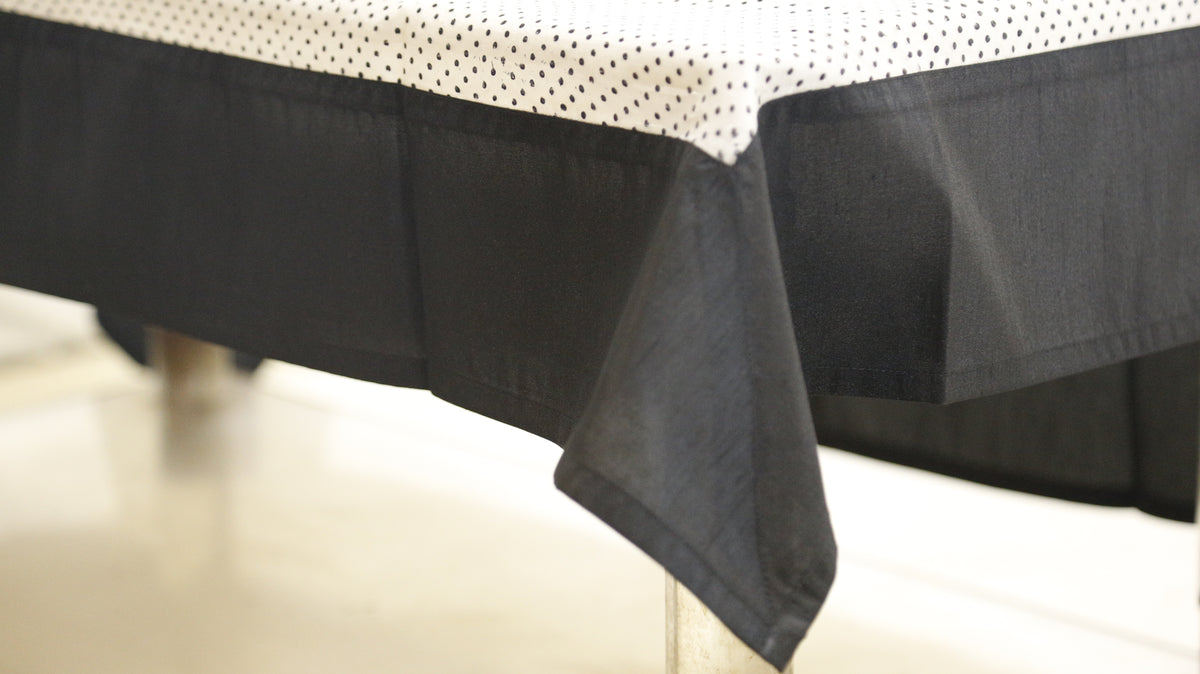 White sheer table cover with a scattered black polka-dot print, set over a solid black underskirt