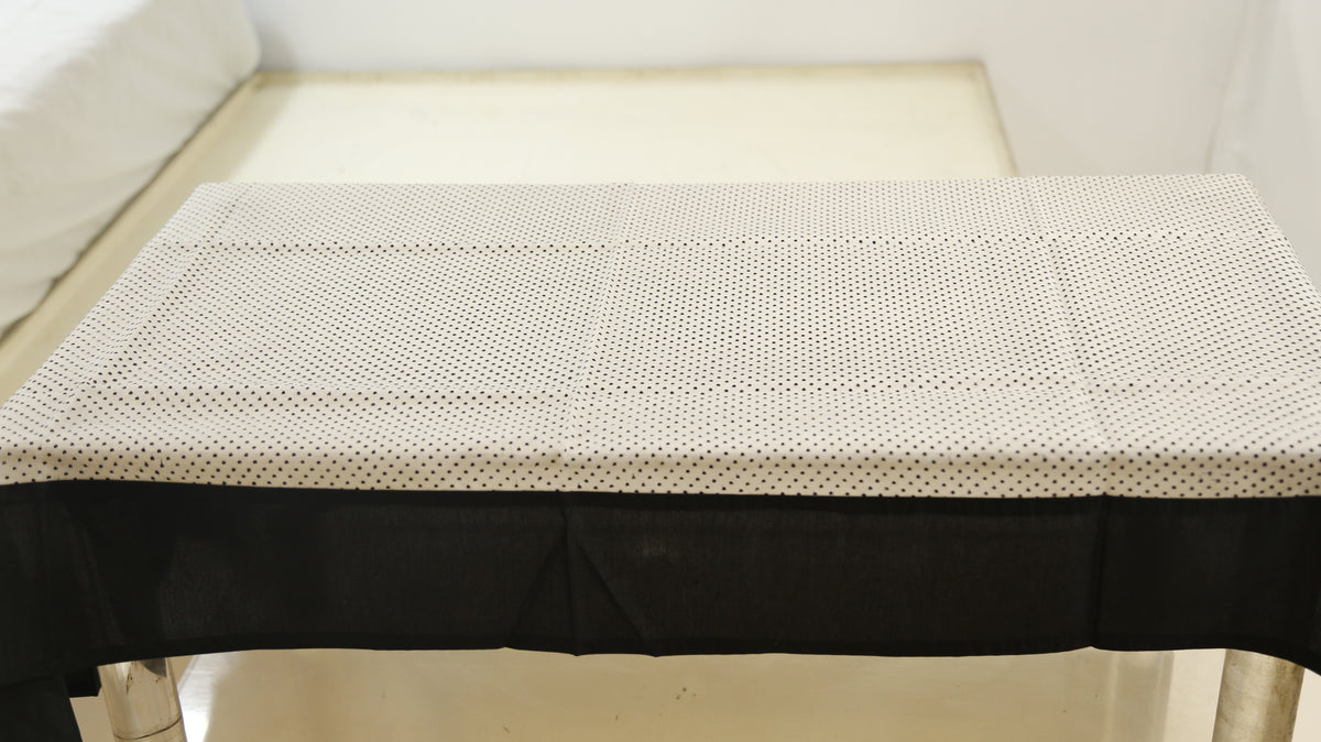 White sheer table cover with a scattered black polka-dot print, set over a solid black underskirt