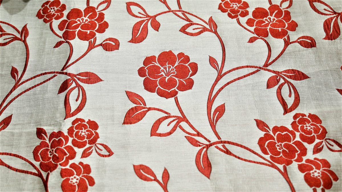 Close up of cream fabric with a red embroidered rose vine on the quilted bedcover