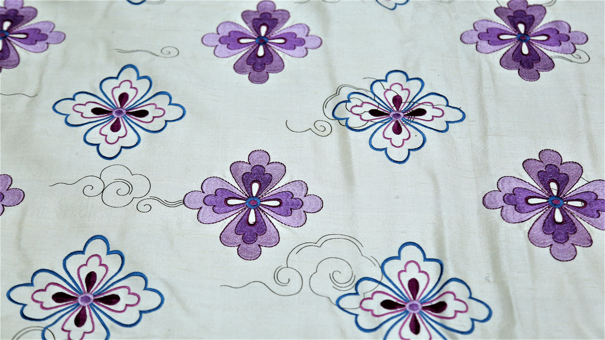 Close up of white polysilk embroidered with purple and blue flowers and fine scrollwork