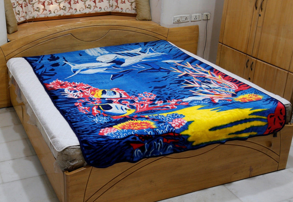 Royal-blue blanket with a printed underwater scene of dolphins, coral reef, and tropical fish, draped over a bed