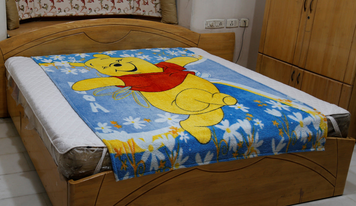 Blue plush blanket with a printed Winnie the Pooh design over a daisy-print border, draped over a bed