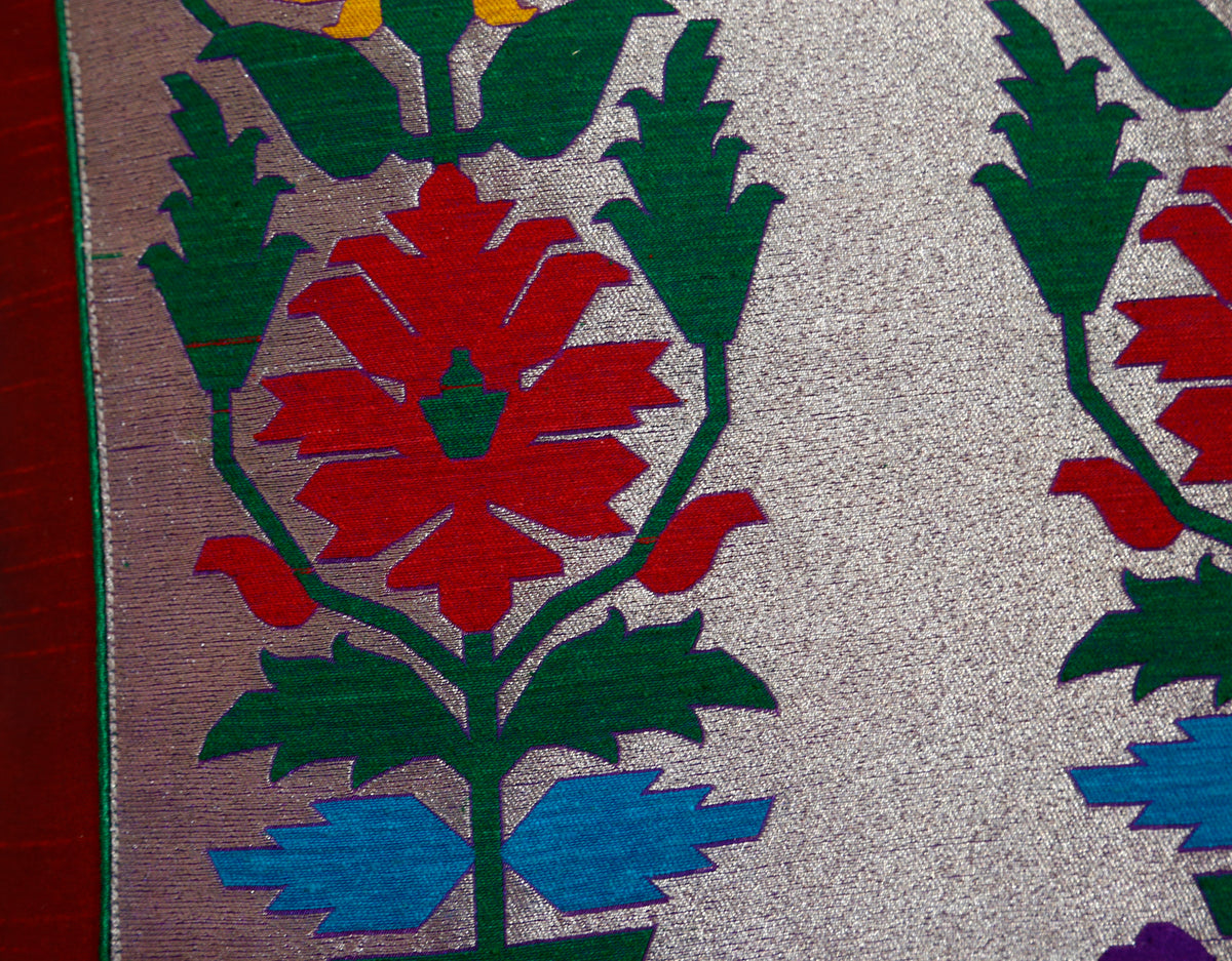 Close-up of the flowering vine woven in orange, red, green and blue on silver brocade