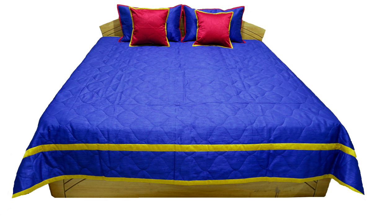 Royal blue quilted bedcover with gold border and crimson cushion covers, straight view
