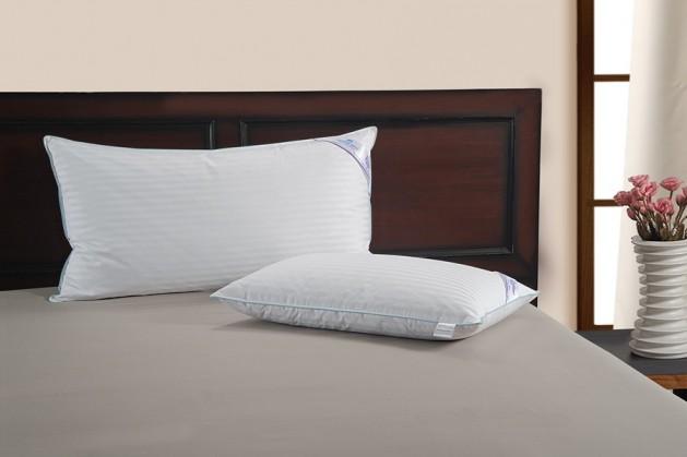 Two Regent satin stripe pillows on a made bed against a dark wooden headboard